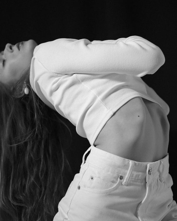 Woman in a dynamic, fluid stretching pose in a minimalist dark studio.